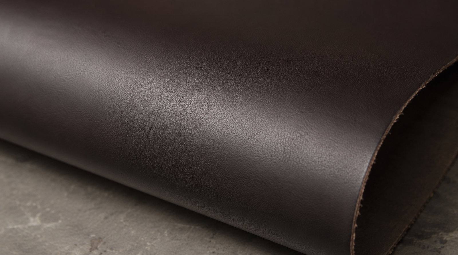 Close-up of a rolled dark brown top grain leather hide showing a smooth, uniform, lightly corrected surface with consistent color and a slight finish sheen